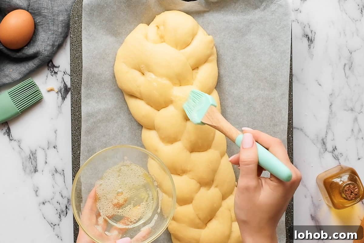 adding egg wash to homemade challah bread before baking.