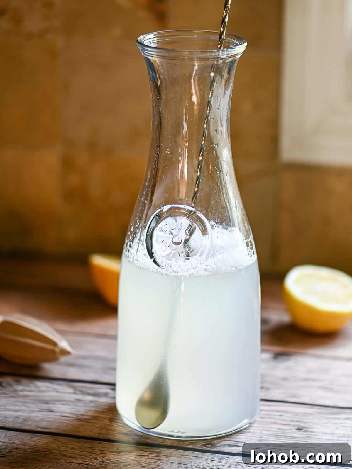 A pitcher with a spoon and lemon slices on a wooden table.