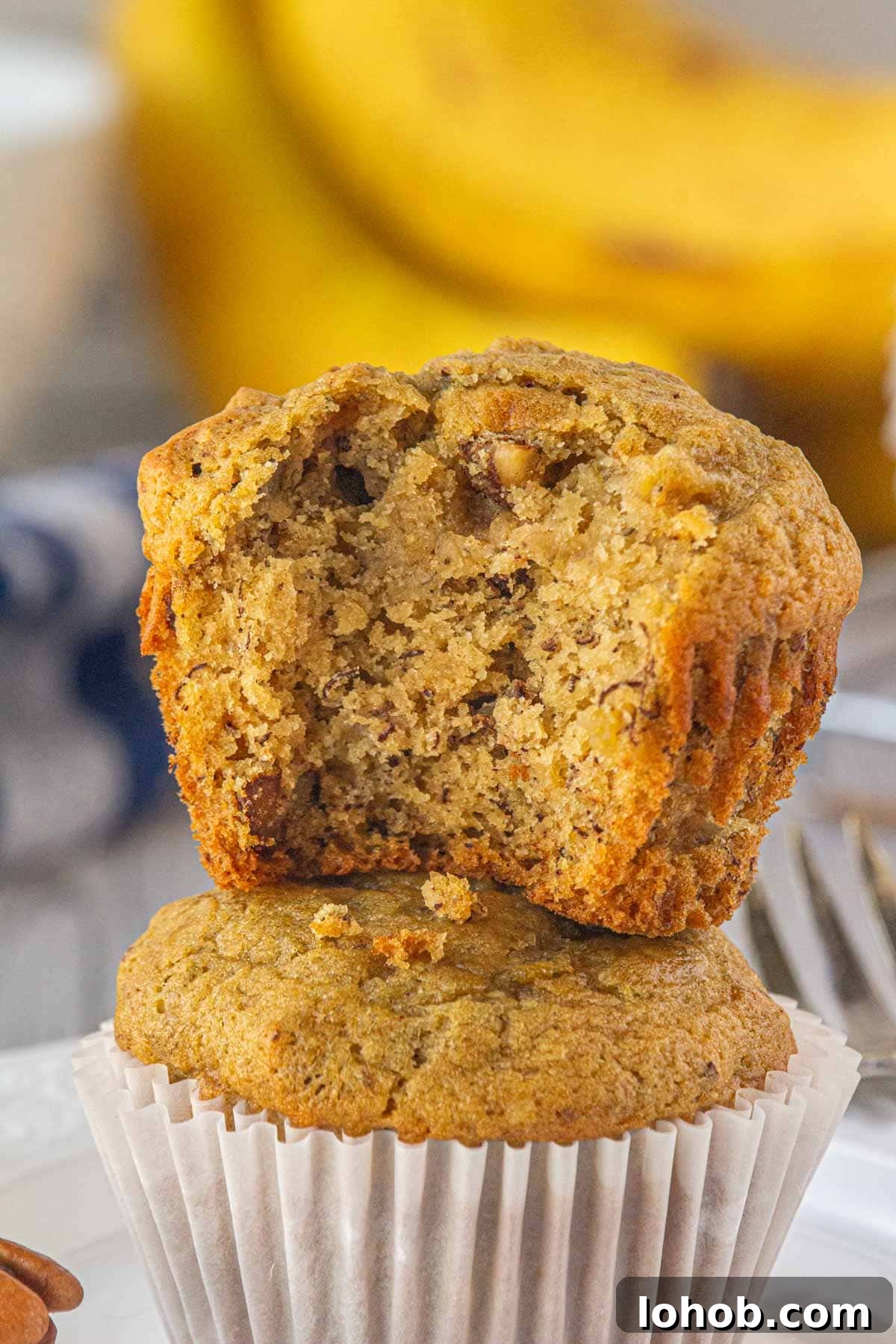 A brown butter banana pecan muffin with a bite taken out stacked on top of another.