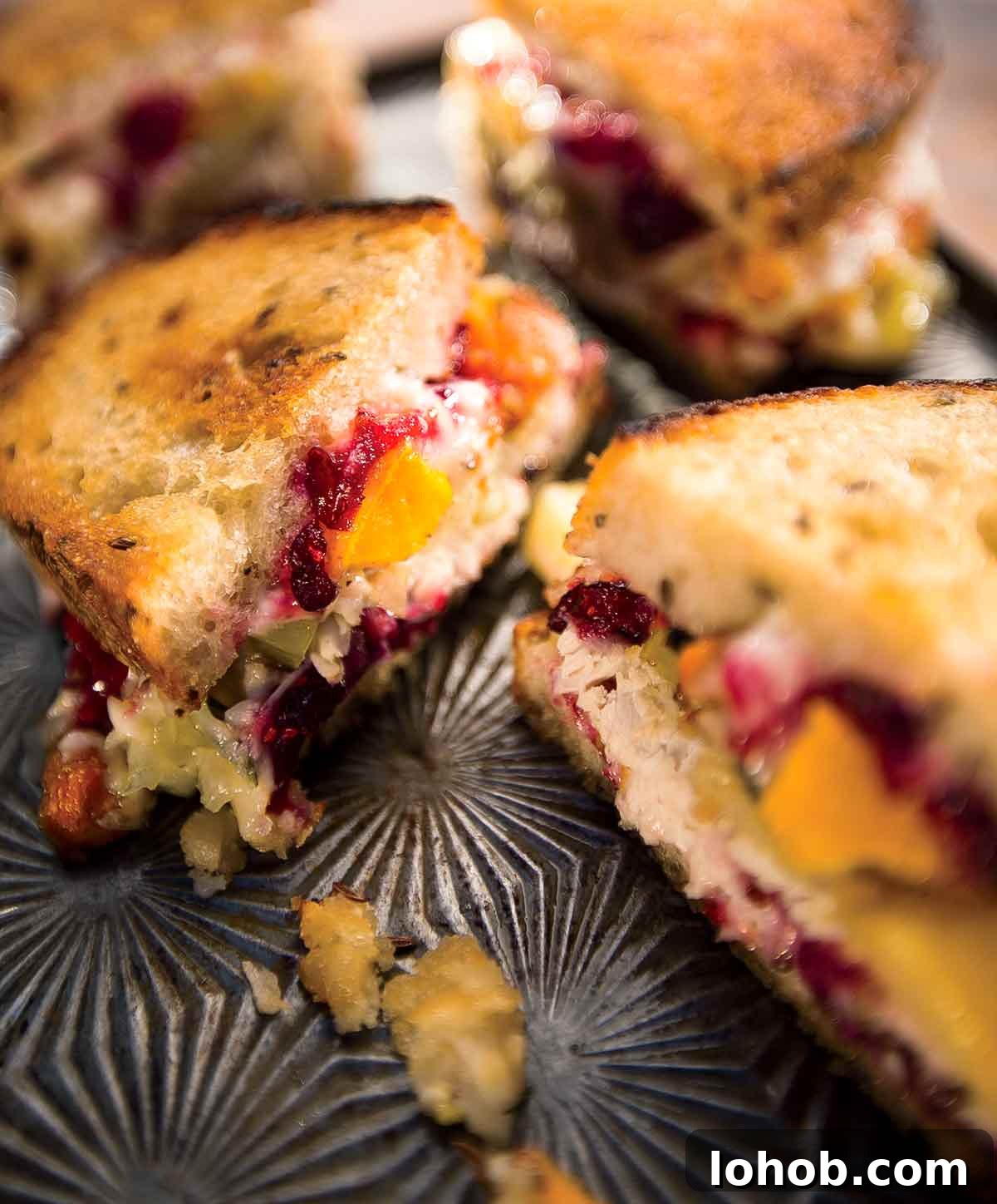 Two hot turkey sandwiches, sliced in half on a tray with pieces of cranberry, avocado, and stuffing lying beside them.