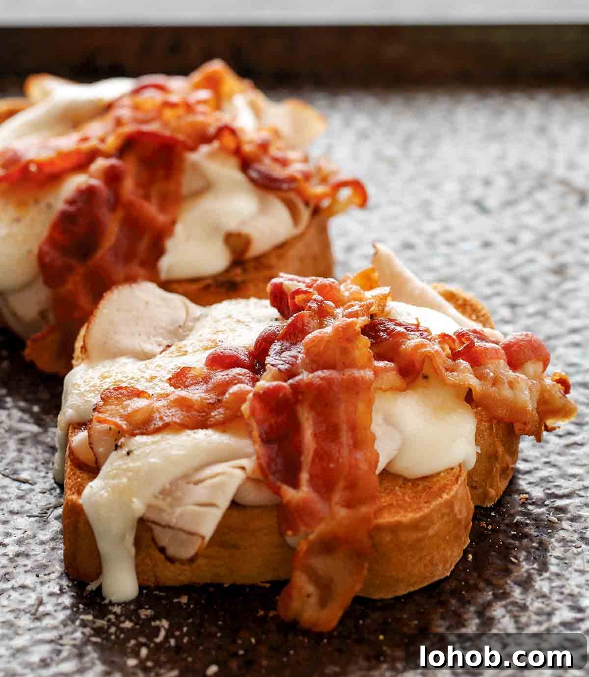 Two open-faced sandwiches topped with turkey, white sauce, and two slices of bacon.