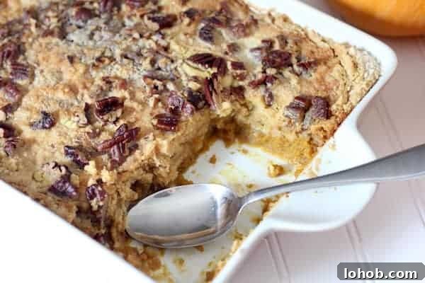 Photo shows a ceramic white pan with a gluten free pumpkin crunch cake in it. Two slices of the cake have been removed, and a spoon rests in the pan.