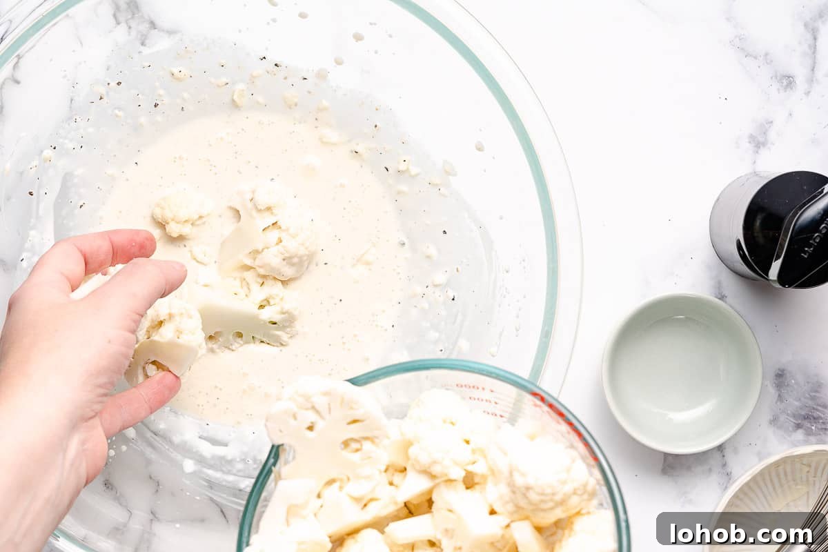 cauliflower florets being added to bowl of mayo dressing