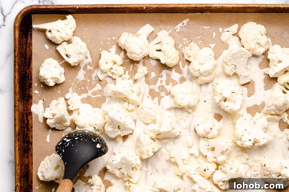 raw cauliflower florets being spread out on baking sheet