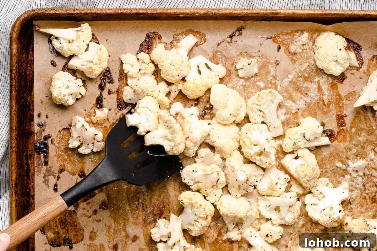 half roasted cauliflower being stirred with spatula on baking sheet