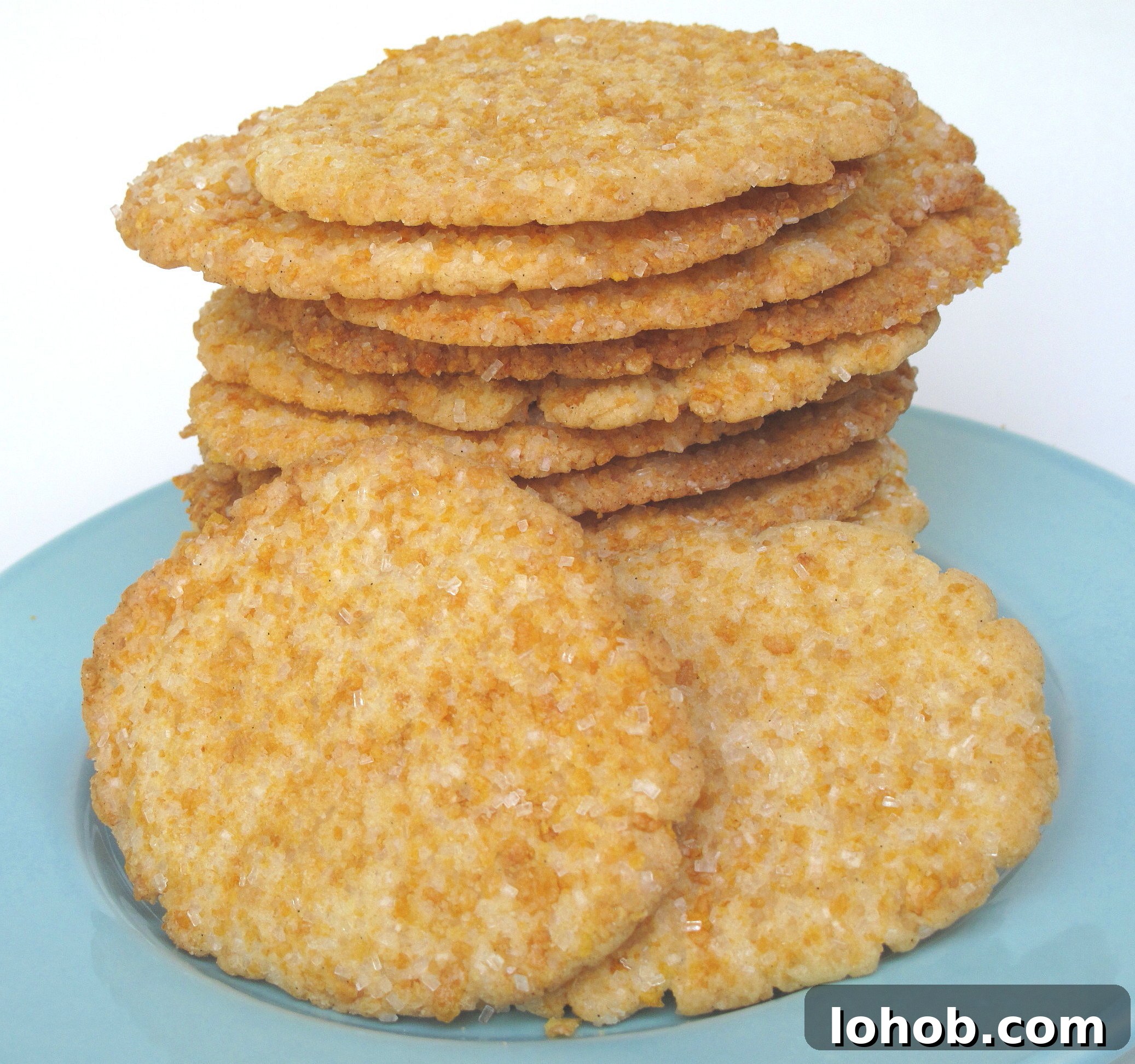 Thin sugar cookies coated in crushed frosted flakes and sugar, stacked on a blue plate.