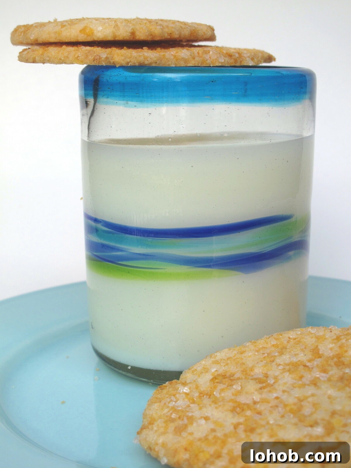 Two thin cookies balanced on the rim of a glass of milk.