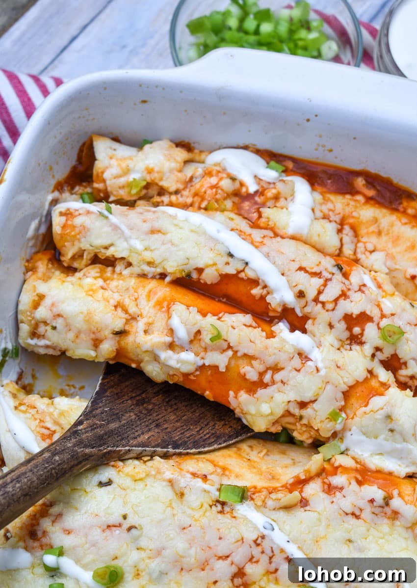 Buffalo Chicken Enchiladas with Creamy Ranch Sauce 5 a wooden spatula scooping buffalo chicken enchiladas out of a white baking dish