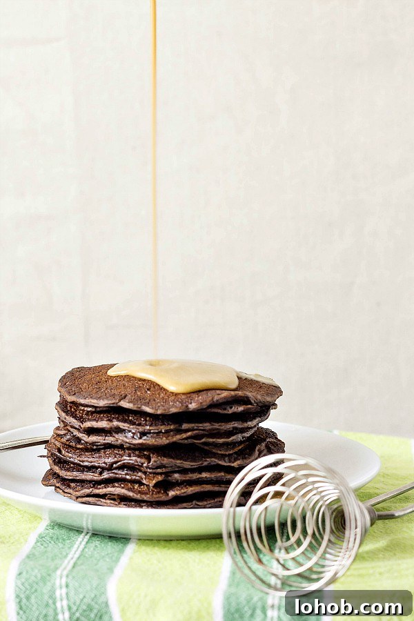 Yeasted Chocolate Chip Pancakes with Rich Cocoa Batter 4 A stack of pancakes with coffee maple syrup being poured over the top.