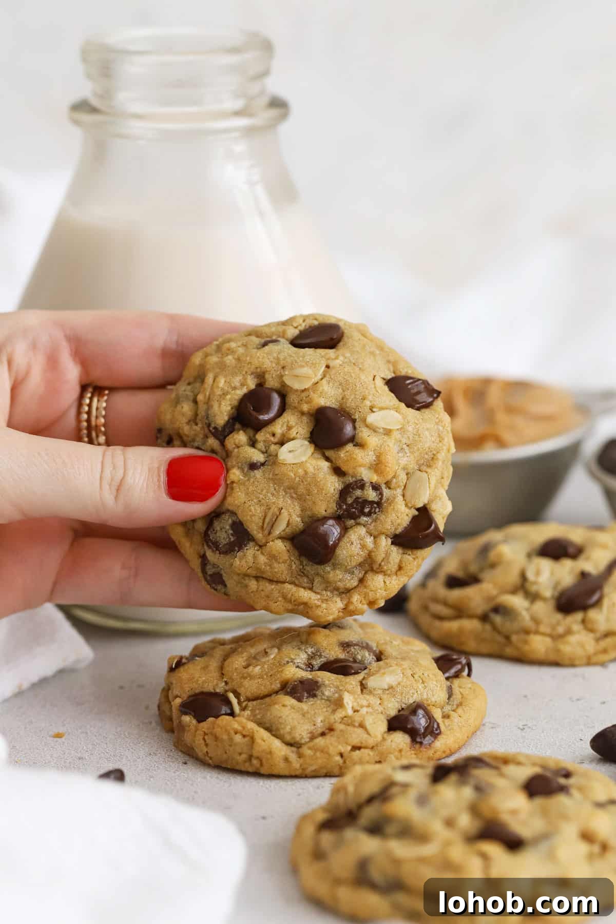 hand holding a gluten-free peanut butter oatmeal chocolate chip cookie in front of a bottle of milk