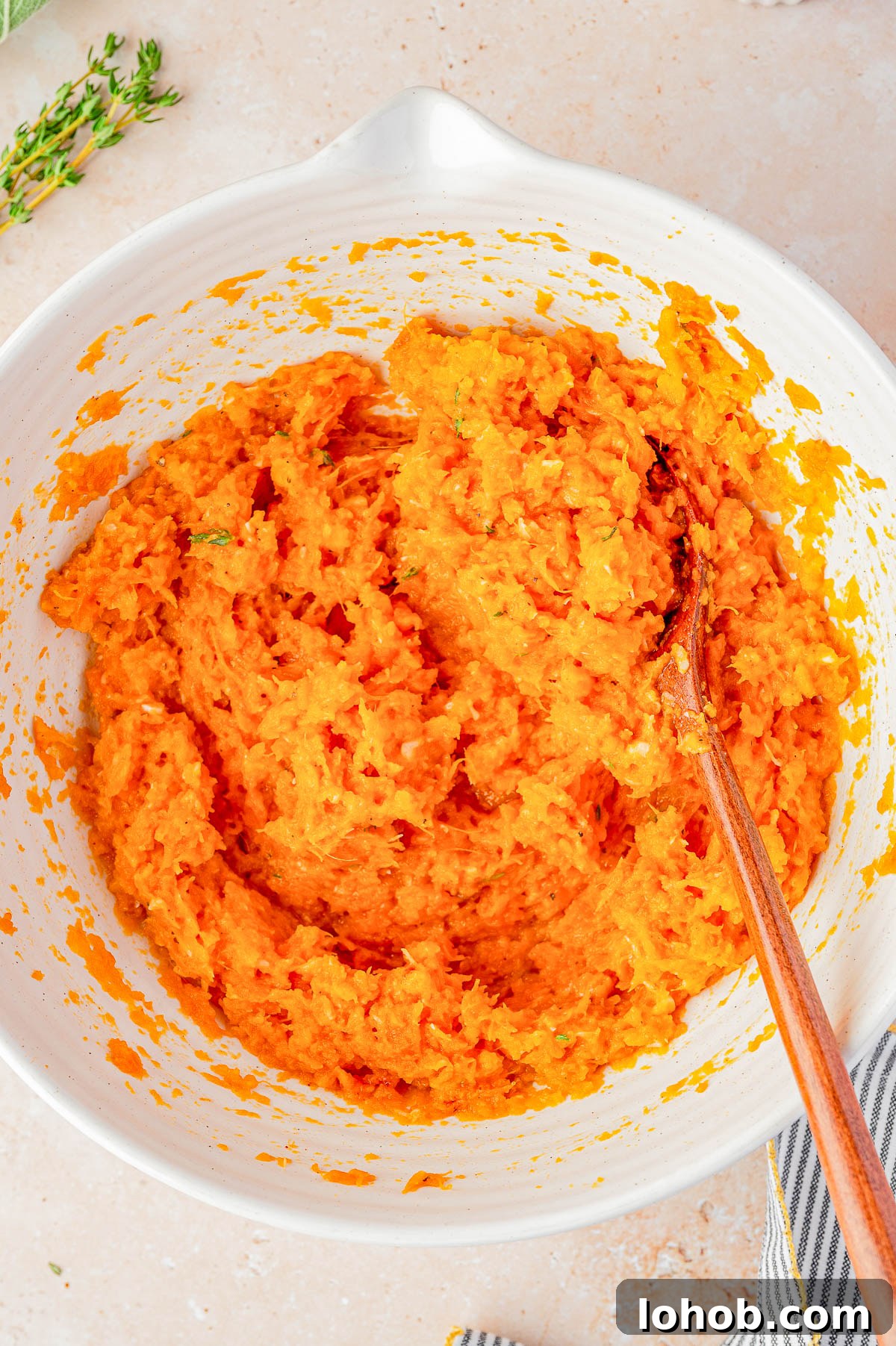 A white mixing bowl filled with a mashed orange mixture being stirred with a wooden spoon.
