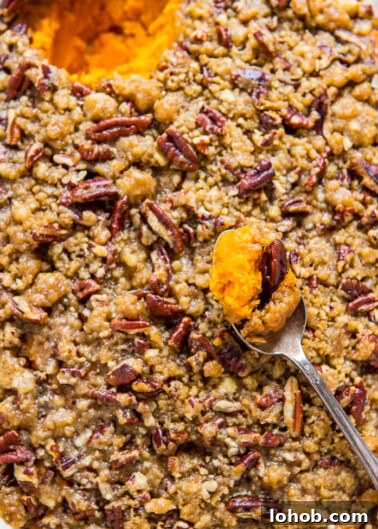 A close-up of a sweet potato casserole topped with pecans and a spoonful being lifted out.