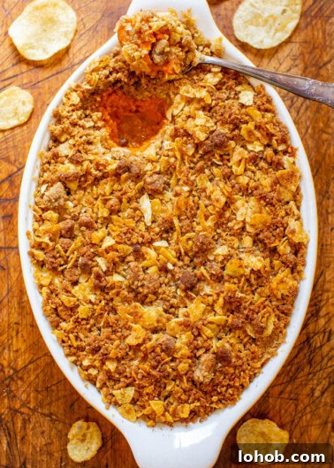 A casserole dish with a crispy golden-brown topping, possibly a gratin or baked dish, with a spoon inside and scattered potato chips around on a wooden surface.