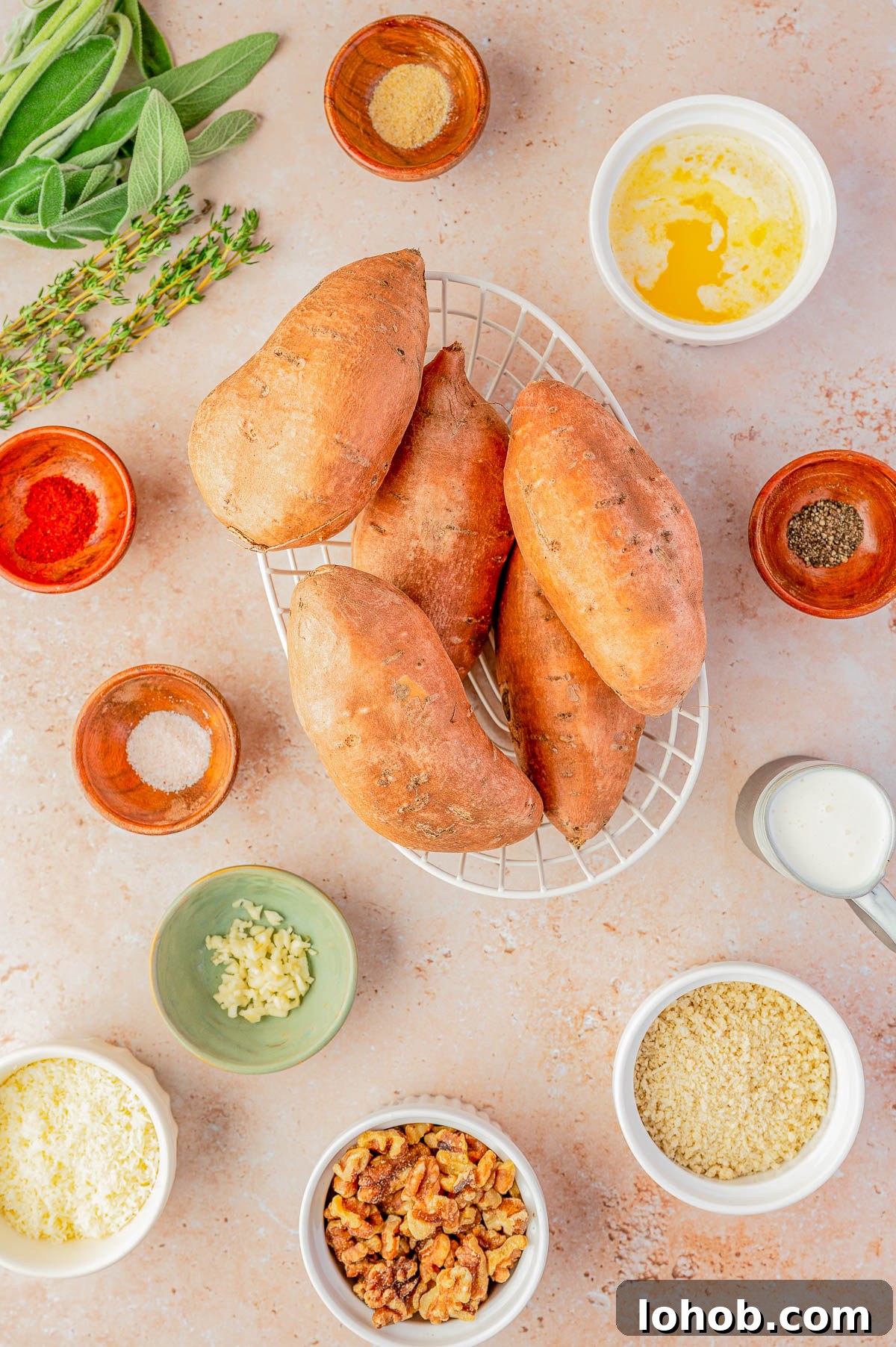 Whole sweet potatoes on a cooling rack surrounded by ingredients in bowls, including herbs, spices, melted butter, milk, garlic, cheese, breadcrumbs, and walnuts.
