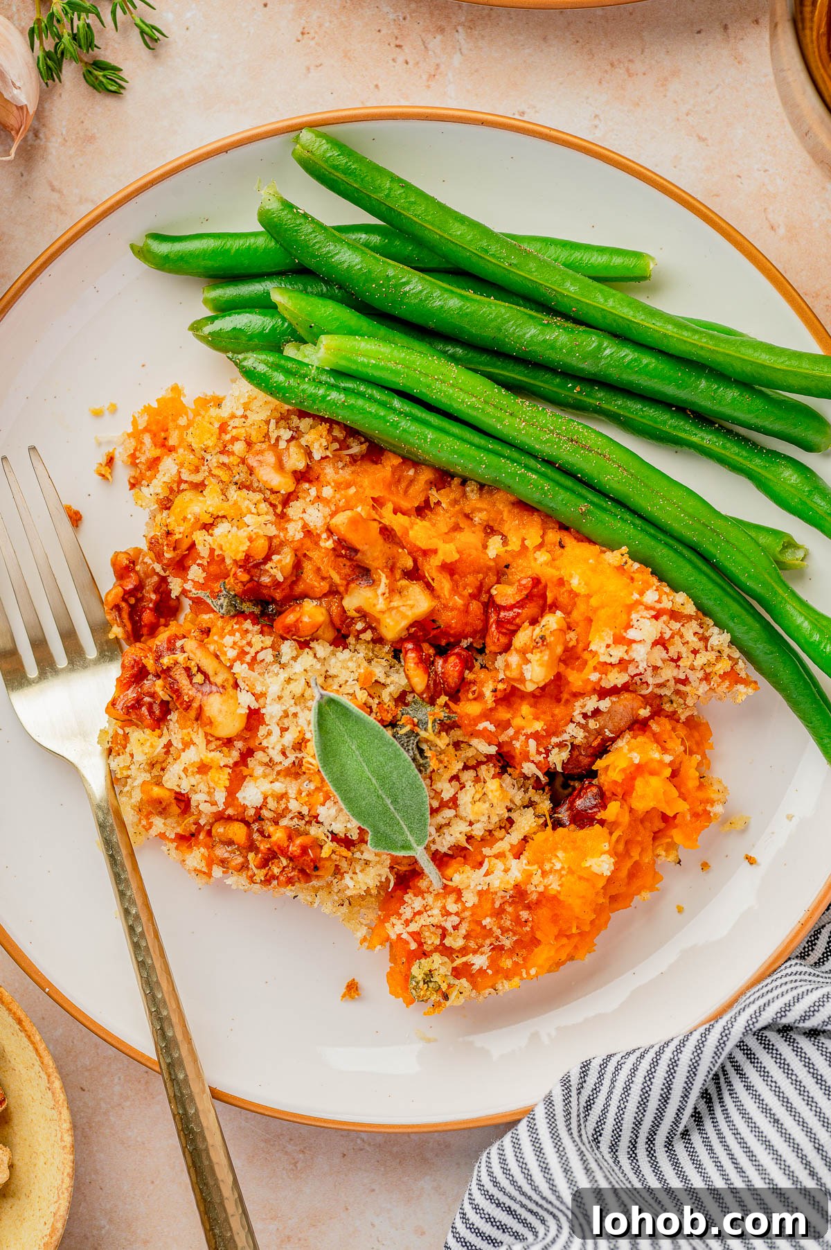 A plate with green beans and a serving of baked casserole topped with breadcrumbs and herbs, with a fork on the side.