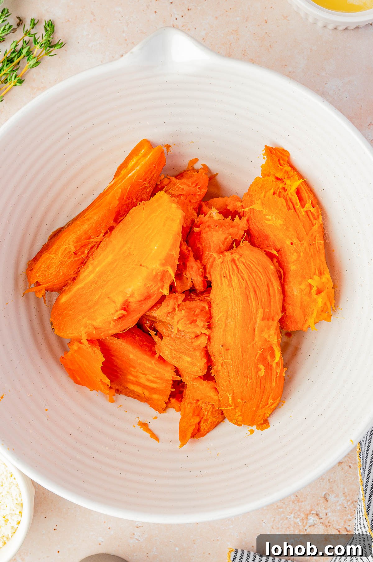 A white bowl containing peeled and cooked sweet potato pieces on a light countertop.
