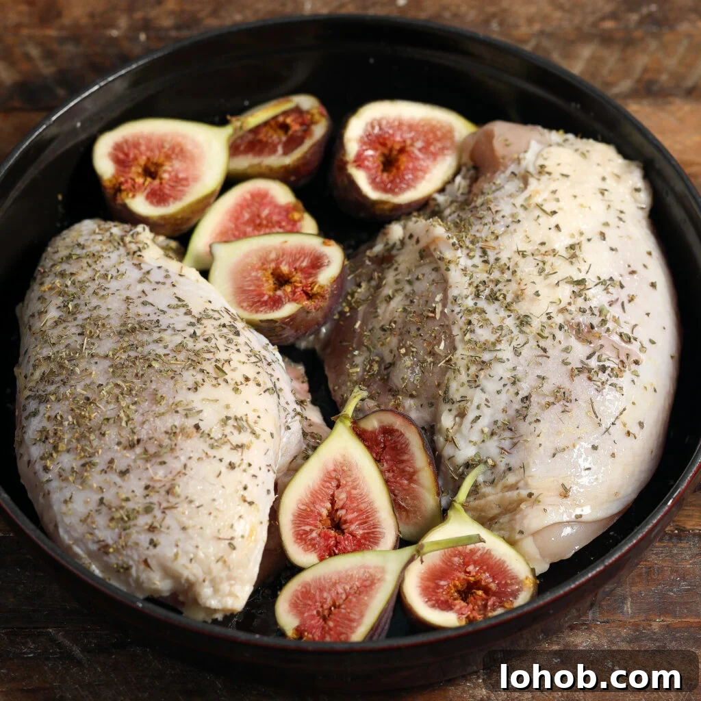 Herb-Roasted Chicken with Caramelized Figs and Balsamic Glaze 3 Raw chicken breasts seasoned with herbs and surrounded by fresh halved figs, ready to become roasted chicken and figs with herbed cheese, arranged in a round black dish on a rustic wooden surface.