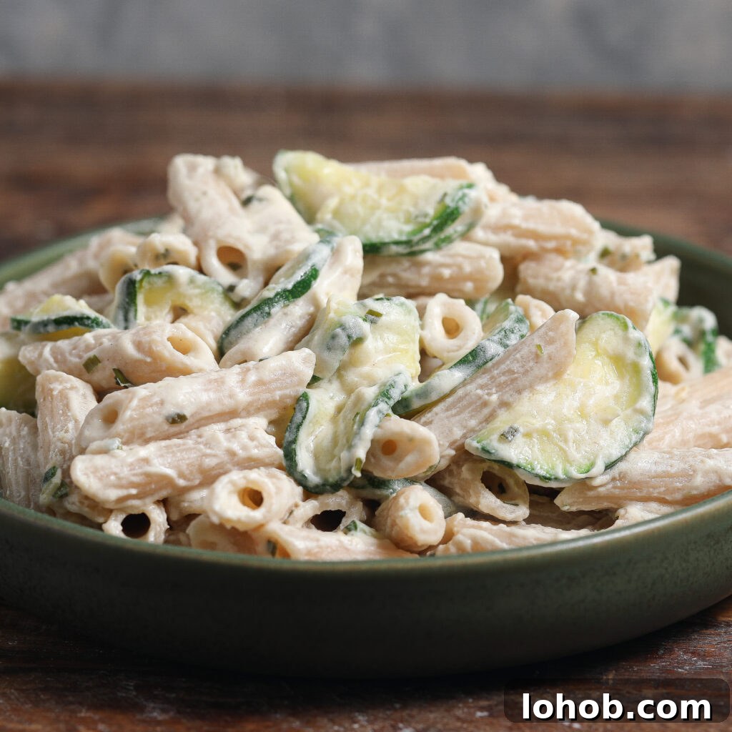 Herb-Roasted Chicken with Caramelized Figs and Balsamic Glaze 5 A green plate filled with penne pasta mixed with creamy white sauce, slices of zucchini, and tender roasted chicken, placed on a wooden surface.