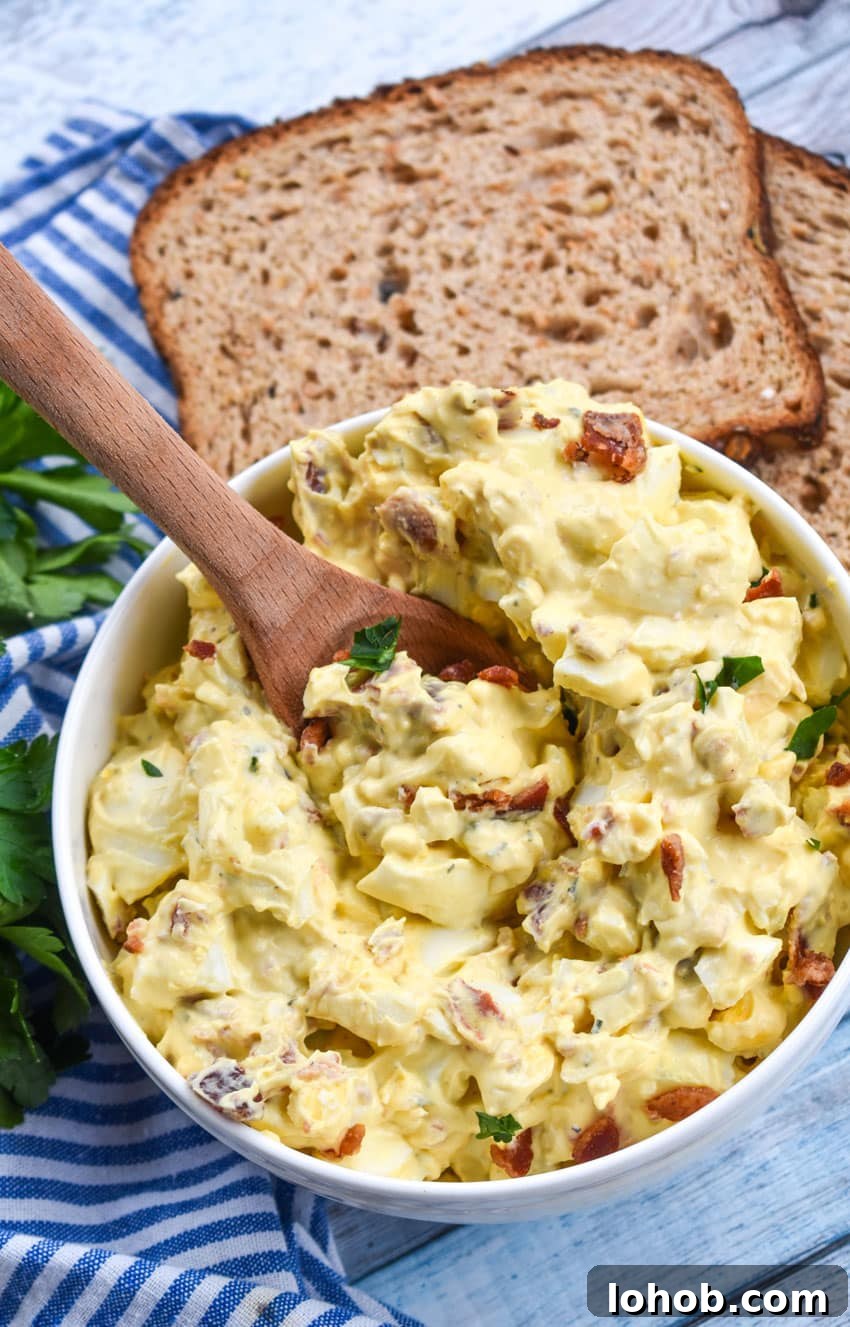 Creamy Bacon Ranch Egg Salad Recipe for Sandwiches & Bowls 4 a wooden spoon scooping bacon ranch egg salad out of a white bowl