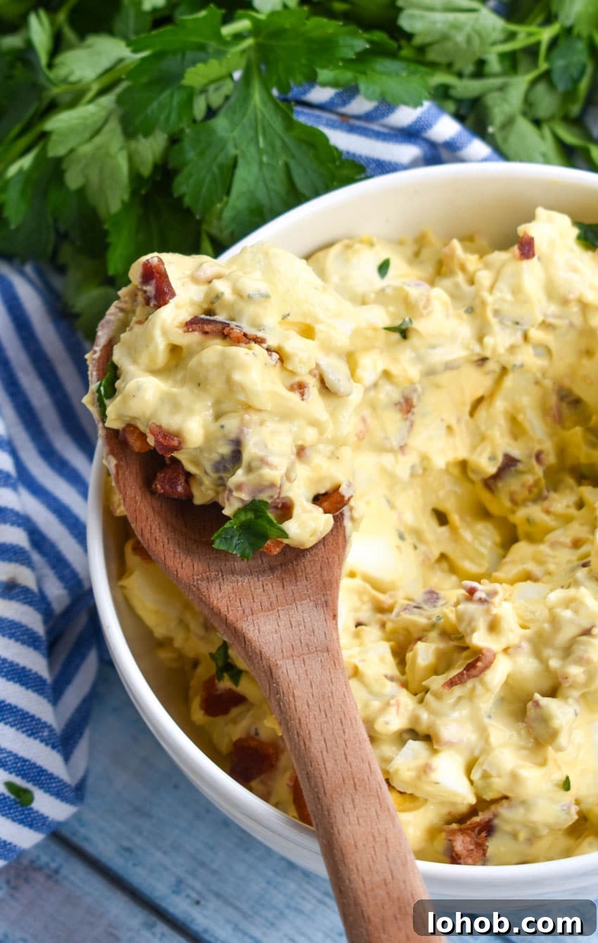 Creamy Bacon Ranch Egg Salad Recipe for Sandwiches & Bowls 5 a wooden spoon holding up a scoop of bacon ranch egg salad
