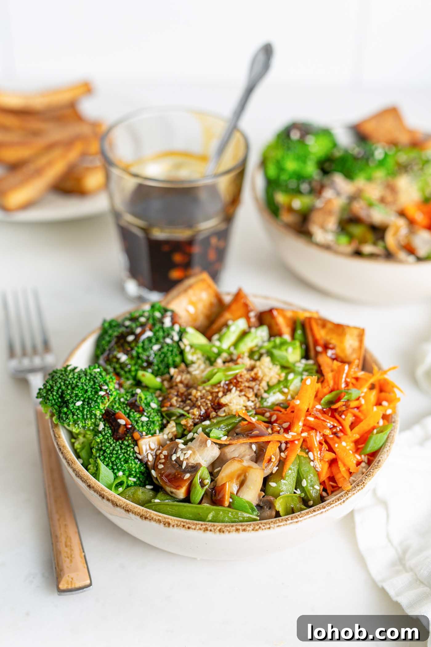 Bowl of quinoa, carrots, peas and mushrooms with teriyaki sauce. Sauce and another bowl in the background.