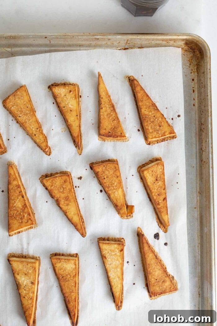 Browned triangles of tofu on a parchment paper-lined baking tray.