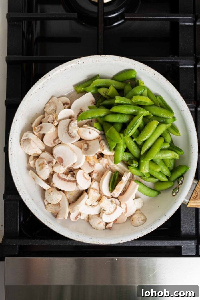 Chopped mushrooms and snap peas cooking in skillet on a gas range stovetop.