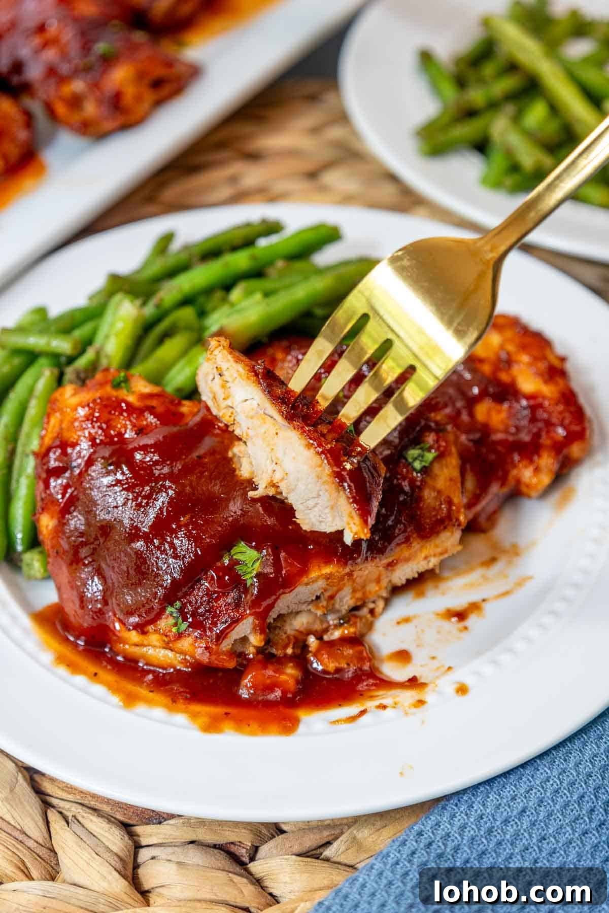 Crispy Oven-Baked BBQ Boneless Chicken Thighs 11 A bite of tender BBQ chicken thigh being lifted by a fork, revealing the juicy inside of the oven baked boneless meat next to green beans.