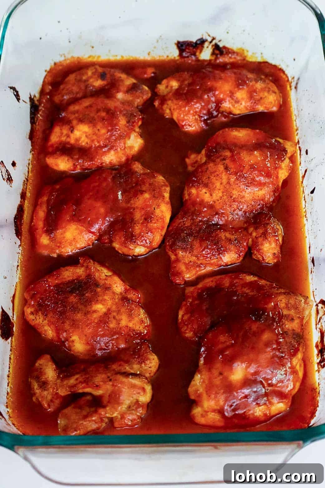 Crispy Oven-Baked BBQ Boneless Chicken Thighs 7 Fully cooked oven baked BBQ boneless chicken thighs resting in a glass baking dish, coated in a thick layer of caramelized sauce.
