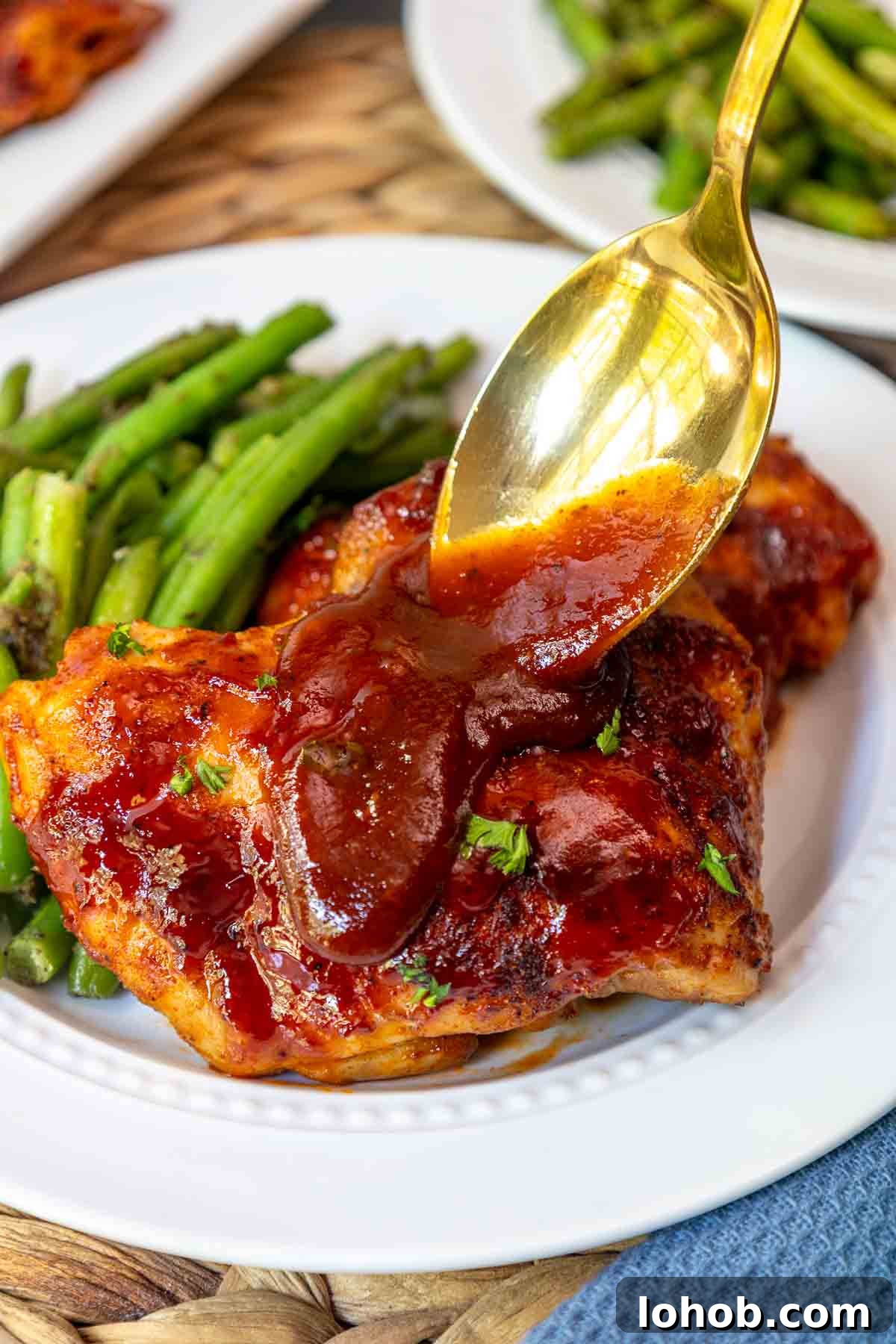 Crispy Oven-Baked BBQ Boneless Chicken Thighs 9 Golden spoon drizzling extra BBQ sauce over a serving of baked boneless skinless chicken thighs.