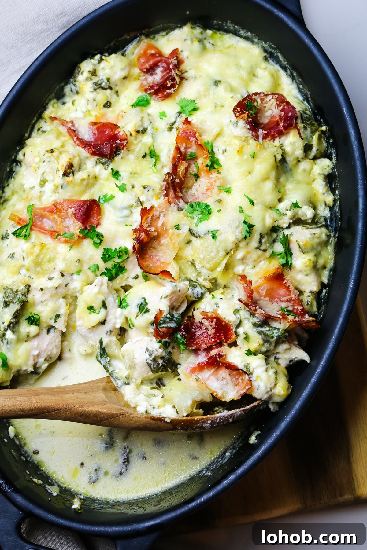 Spinach, Chicken & Artichoke Casserole Recipe with Light Cream Sauce 2 chicken artichoke casserole in black baking dish with prosciutto pieces on top with green parsley.