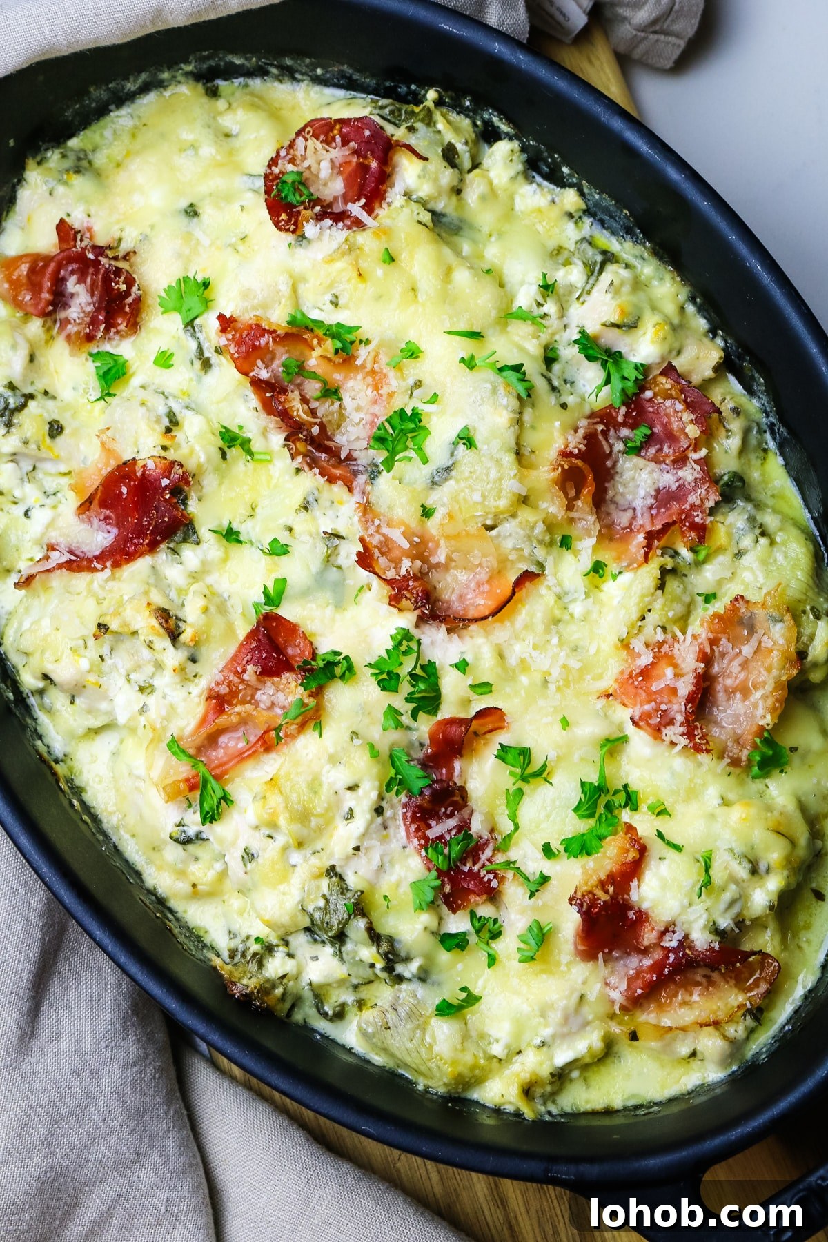 Spinach, Chicken & Artichoke Casserole Recipe with Light Cream Sauce 5 chicken artichoke casserole in a black oval baking dish with fresh parsley garnish.