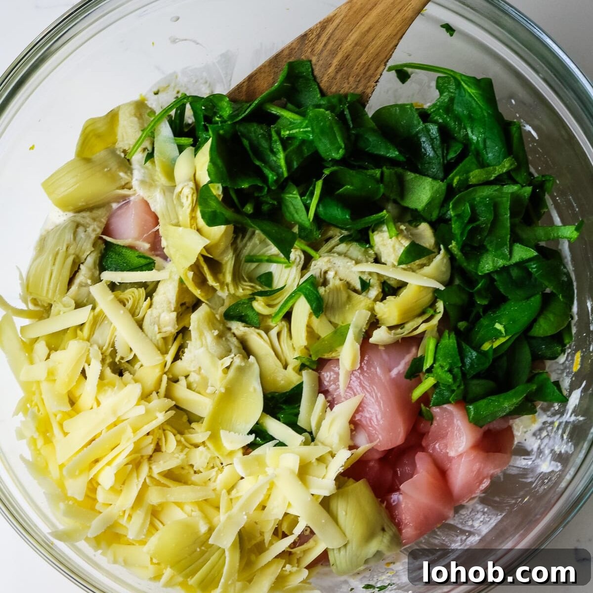 Spinach, Chicken & Artichoke Casserole Recipe with Light Cream Sauce 8 in a glass bowl, spinach, artichoke hearts, grated cheese, and raw chicken.