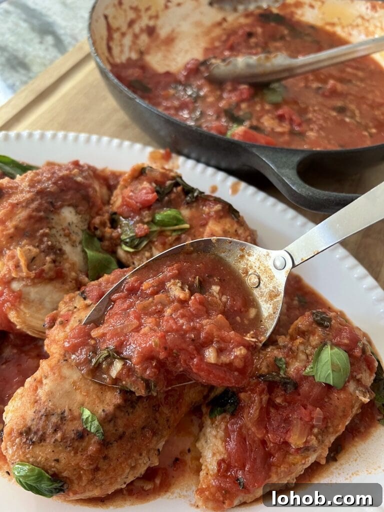 One-Pan Chicken Pomodoro Recipe for Quick Weeknight Dinners 17 Spooning additional pan sauce over the plated chicken pomodoro in white serving platter.