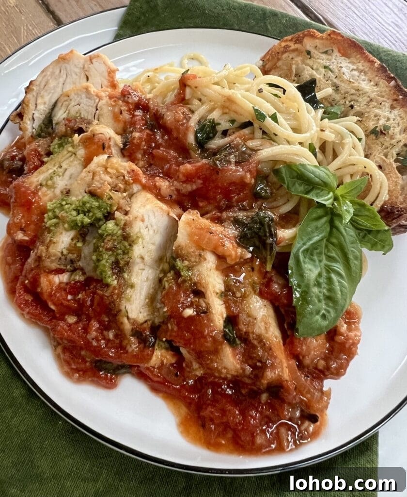 One-Pan Chicken Pomodoro Recipe for Quick Weeknight Dinners 3 Sliced Pomodoro Chicken on white dinner plate with spaghetti, bread, basil garnish and a little pesto.