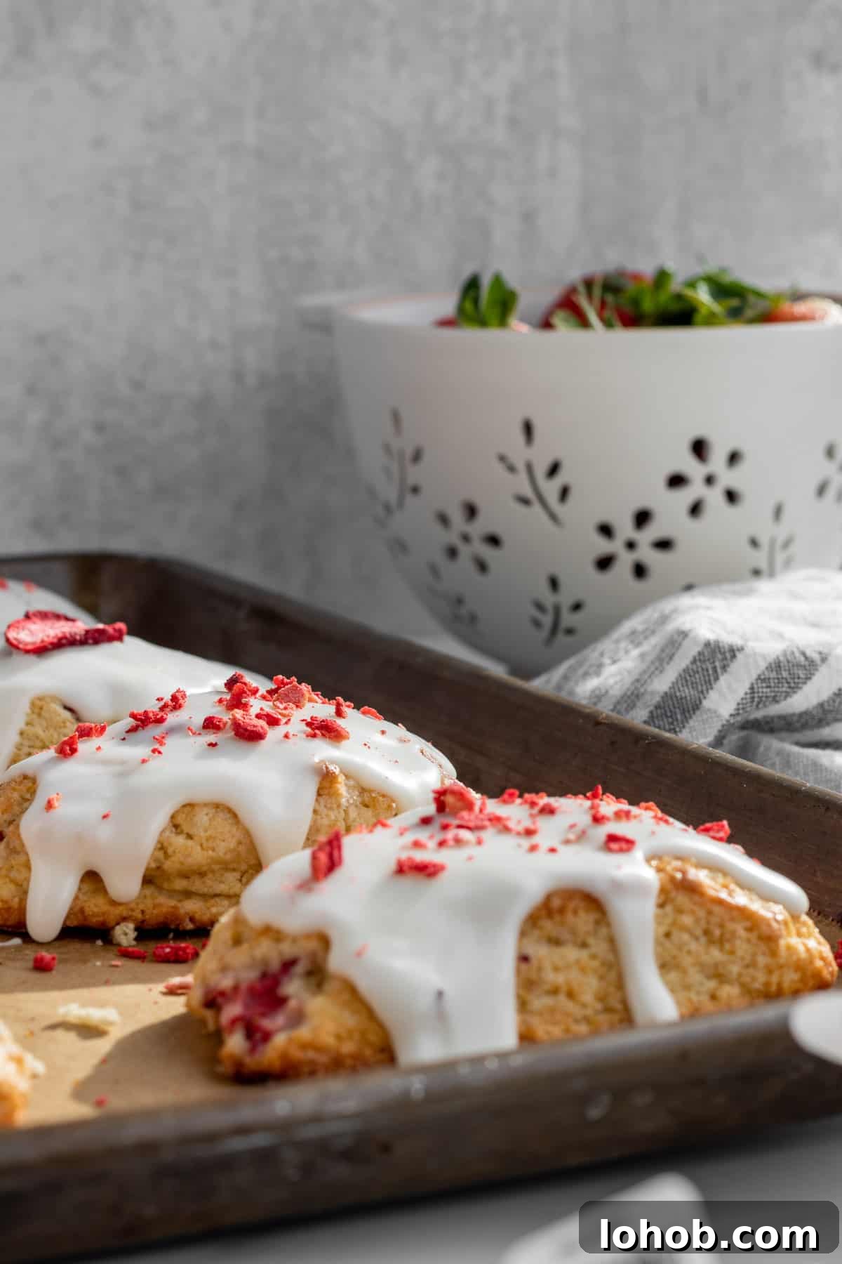 Strawberry Cream Scones with Vanilla Glaze 8 strawberry and cream scones on a baking sheet with a colander of strawberries in the background