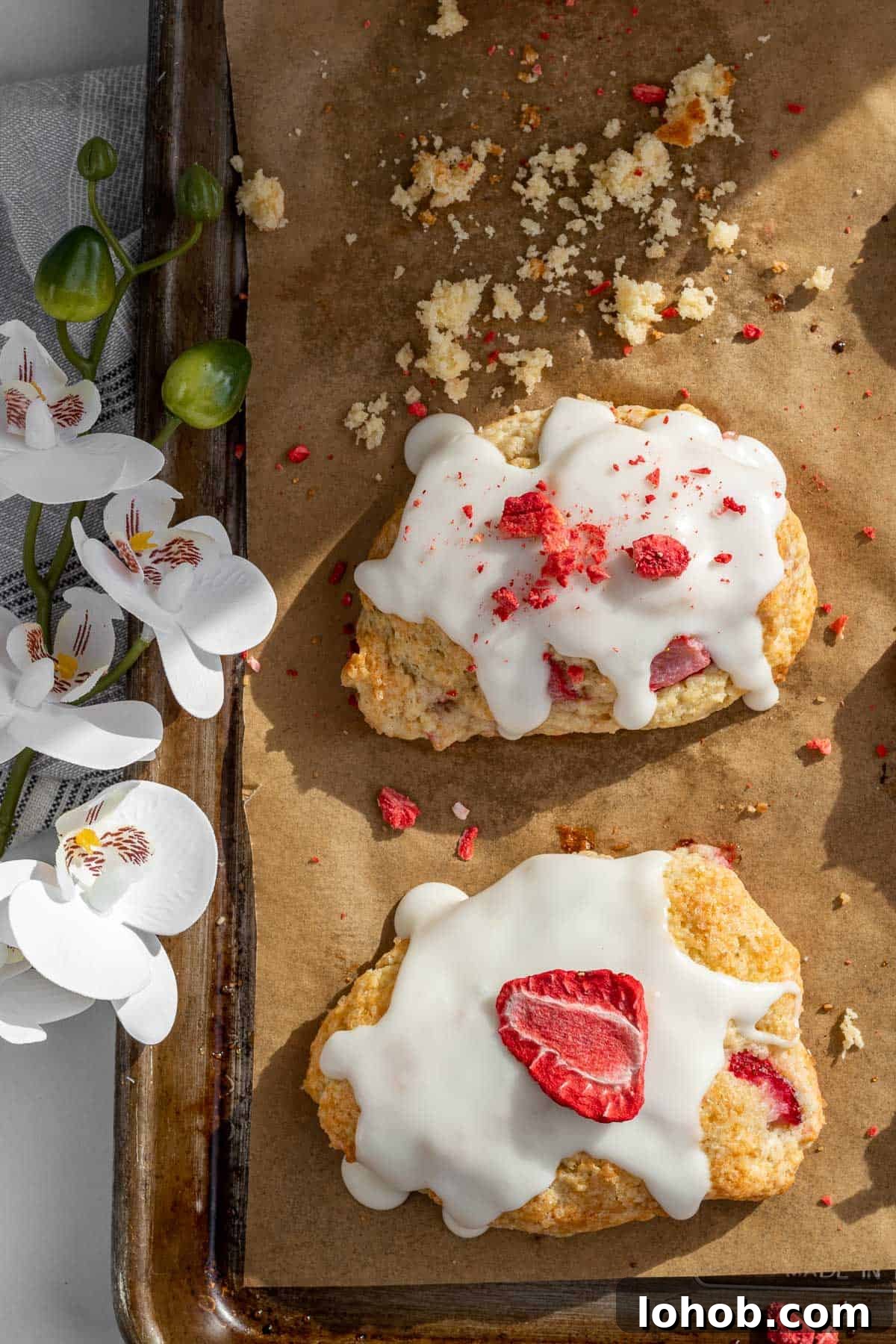 Strawberry Cream Scones with Vanilla Glaze 9 strawberry scones on a baking sheet with orchids next to it