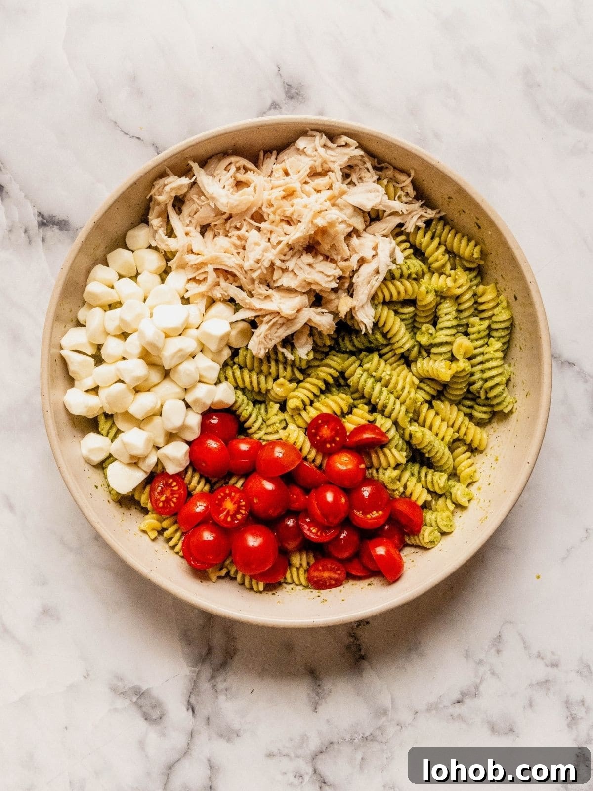 Grilled Chicken Pesto Pasta Salad with Sun-Dried Tomatoes 8 Large bowl with pasta tossed in pesto, layered with shredded chicken, mozzarella balls and cherry tomato slices.