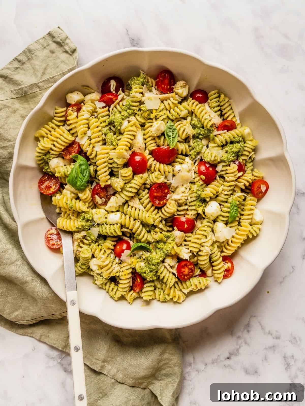 Grilled Chicken Pesto Pasta Salad with Sun-Dried Tomatoes 9 Chicken and pesto pasta salad in a large serving bowl garnished with basil leaves and shaved parmesan.