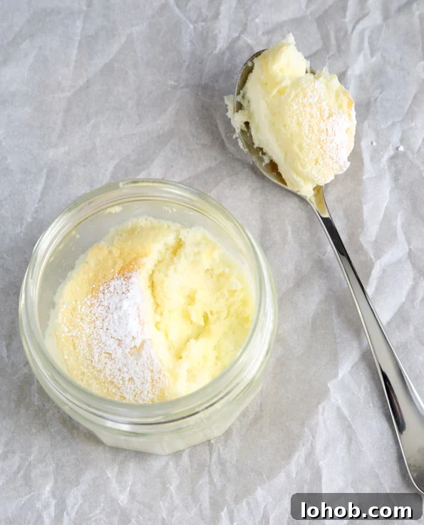 A miniature lemon cake in a jar with powdered sugar and a spoonful taken