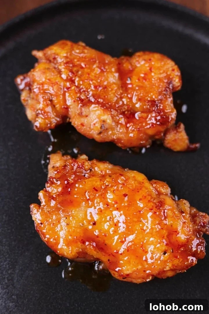 Crispy Honey Garlic Chicken Thighs — One-Pan Recipe 2 Crispy honey garlic chicken thighs served on a black platter with a glossy sticky glaze.
