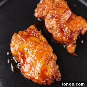 Crispy honey garlic chicken thighs served on a black platter with a glossy sticky glaze.