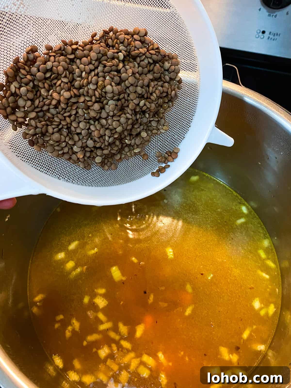 Hearty Vegan Lentil and Vegetable Noodle Soup Recipe 8 Photo of the pan with stock added and lentils being added from a sieve above.