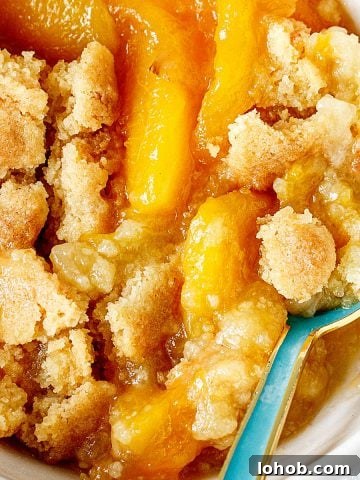 Close view of peach dump cake serving in white bowl with a teal spoon.