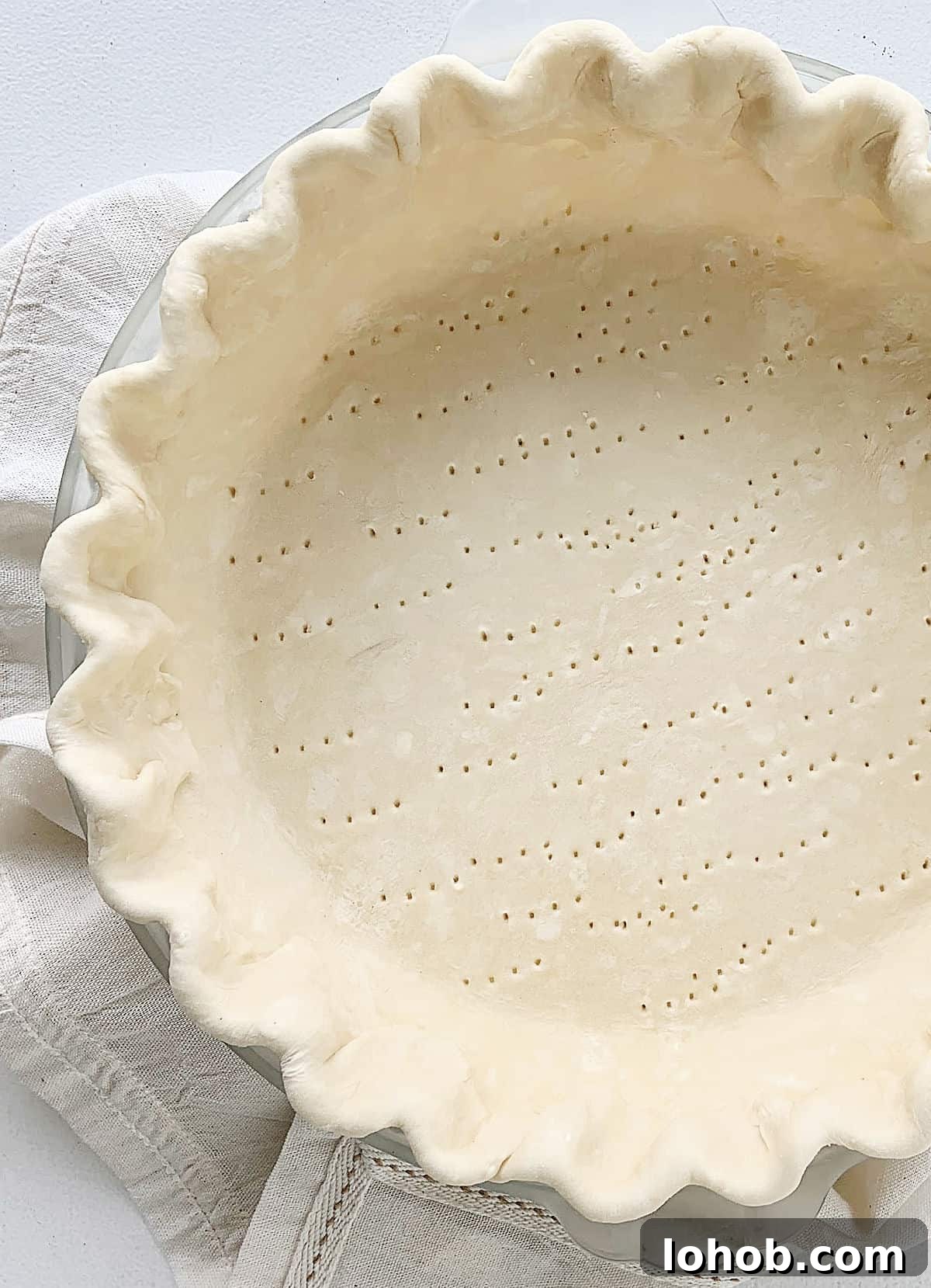 Perfect Peach Pie with Buttery Crumb Topping 5 Partial view of unbaked pie crust with crimped edges on a white linen and table.