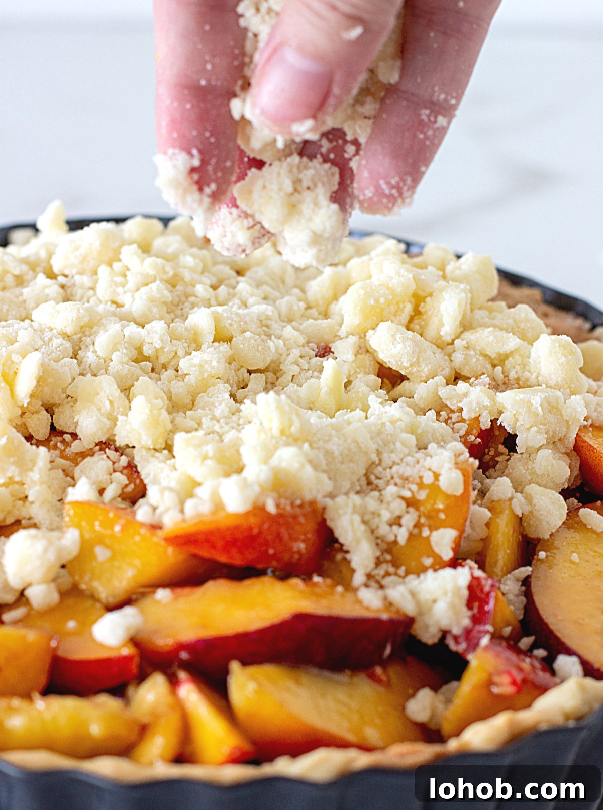 Perfect Peach Pie with Buttery Crumb Topping 7 Hand adding crumble to peaches in pie metal pan.