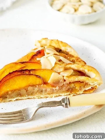 Almond cream peach tart slice on a white plate. Silver fork. White background.