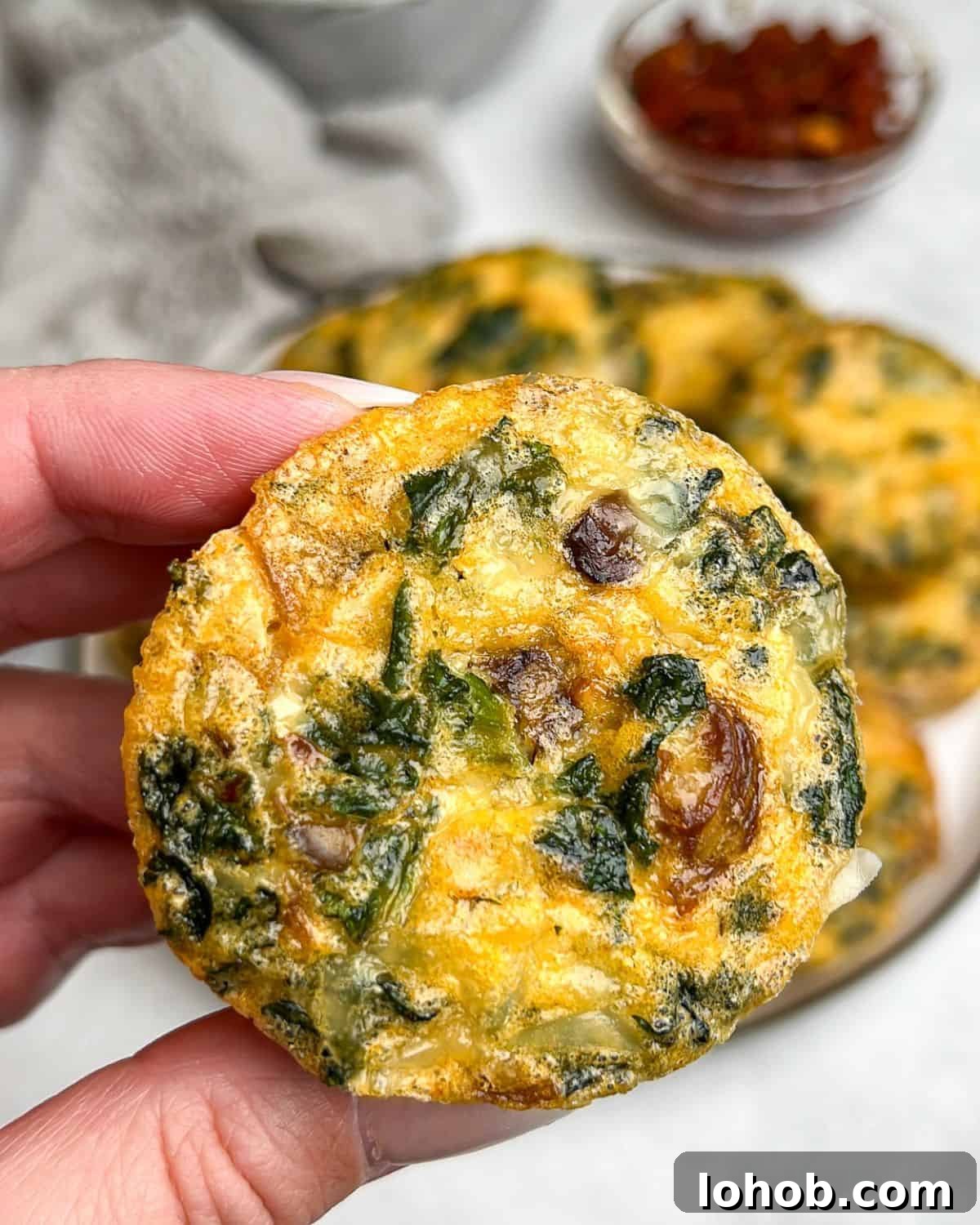 These kale and mushroom egg bites bring all the fluffy, protein-packed goodness of the Starbucks original, with a few flavor-packed upgrades! A hand holding a kale and mushroom egg bite up to the camera.