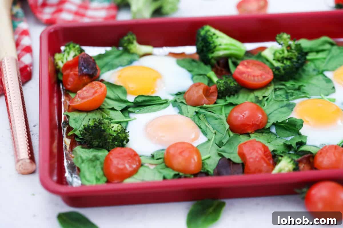 Sheet pan with cooked eggs, spinach, tomatoes, broccoli, and bacon.