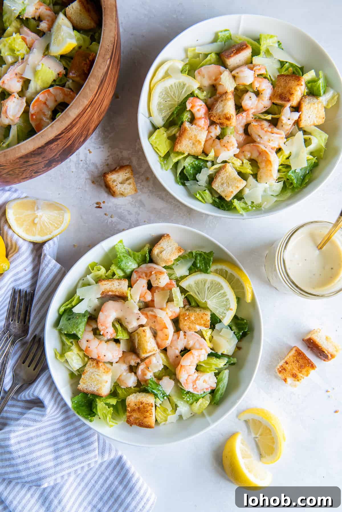 Grilled Shrimp Caesar Salad with Crispy Parmesan Croutons 2 Two bowls of Shrimp Caesar Salad next to a salad bowl and mason jar filled with dressing.